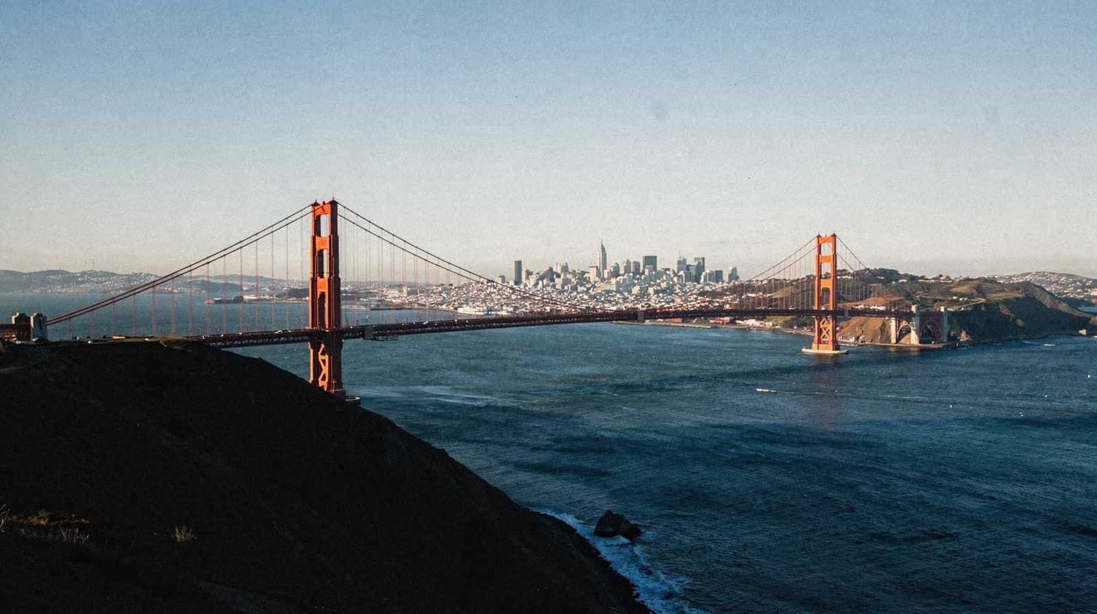 The Ferry Building's clock tower on the Embarcadero, photographed at dusk as a streetcar rolls past.